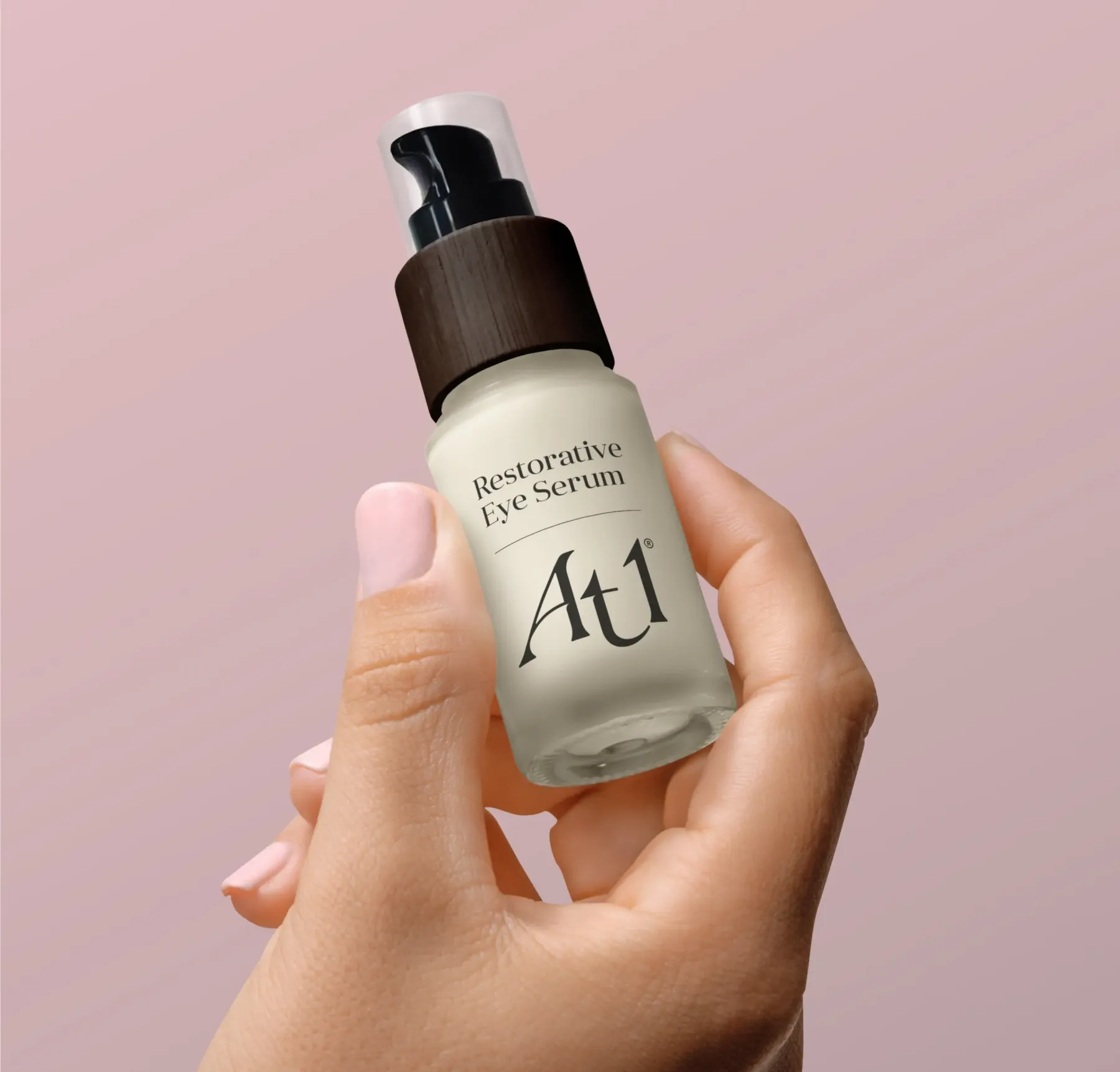 A female hand with pink nail varnish holding a bottle against a pink background