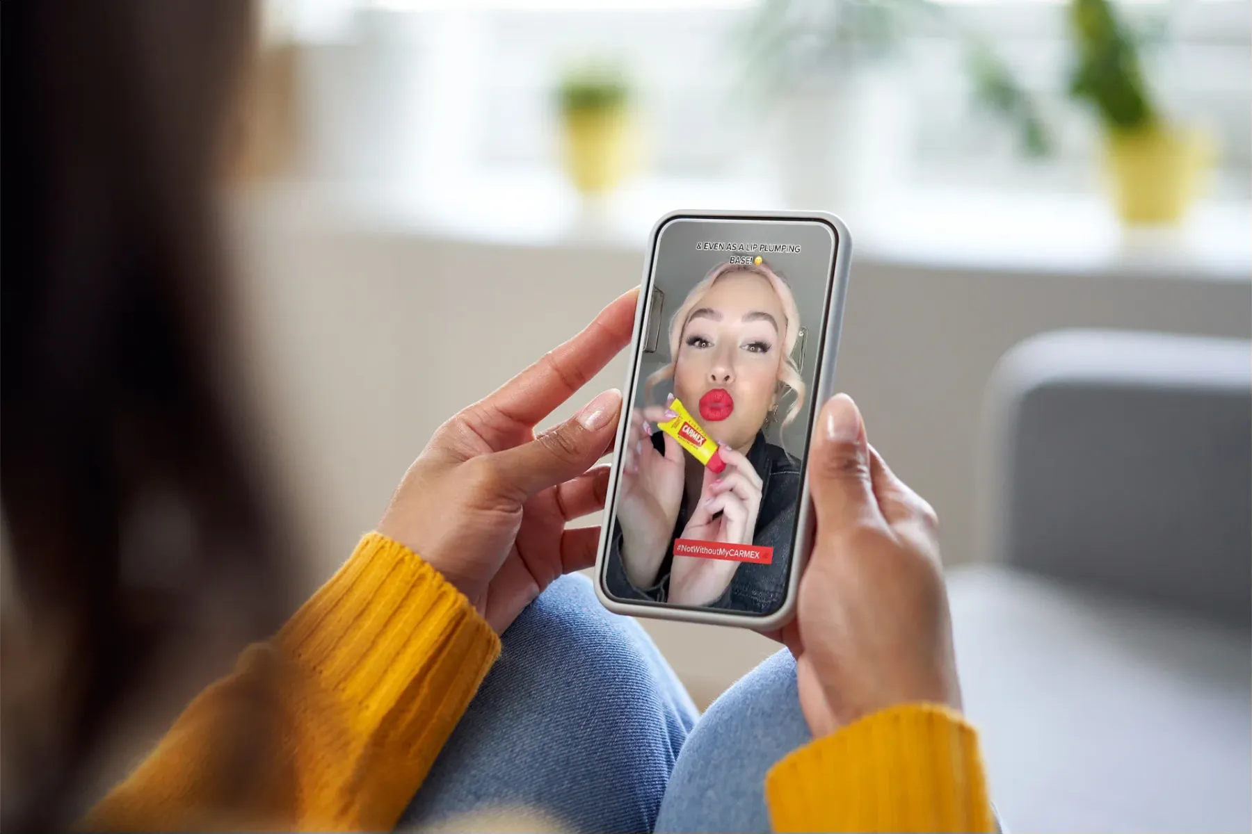 view over the shoulder of woman holding a phone, watching Carmex socal video